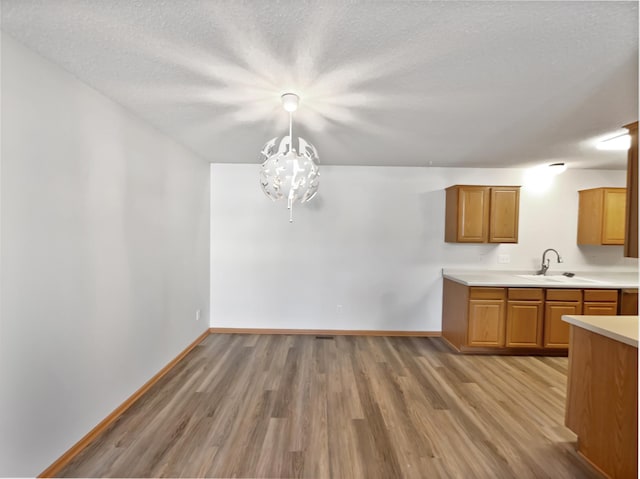 kitchen featuring light wood finished floors, light countertops, brown cabinets, an inviting chandelier, and a sink