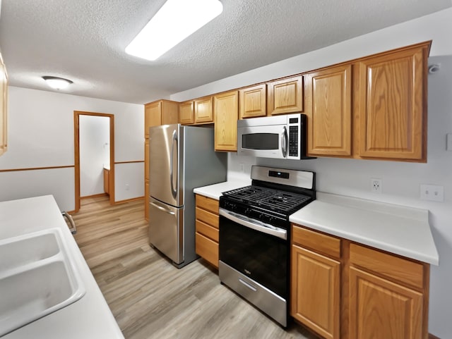 kitchen featuring light wood finished floors, light countertops, stainless steel appliances, a textured ceiling, and a sink