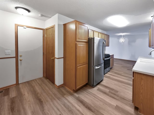 kitchen featuring a sink, stainless steel appliances, a textured ceiling, and light wood-style flooring