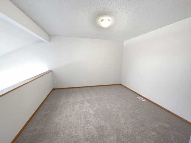 carpeted spare room featuring visible vents, baseboards, a textured ceiling, and vaulted ceiling with beams