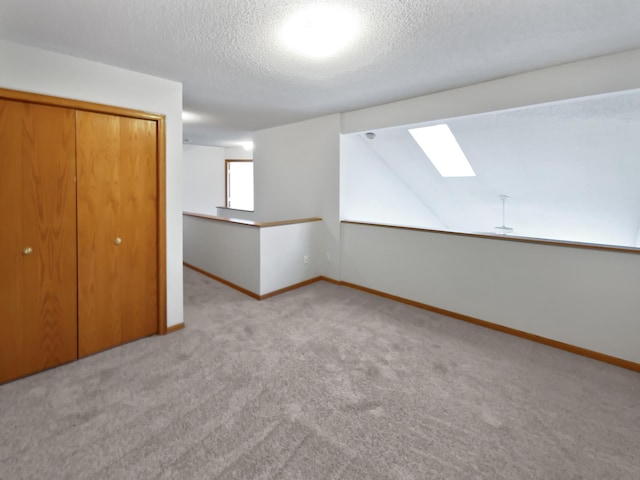 unfurnished bedroom featuring baseboards, a skylight, a closet, a textured ceiling, and carpet flooring