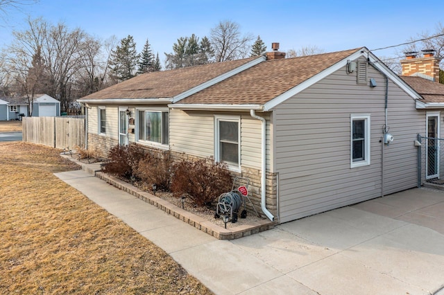 exterior space featuring fence, roof with shingles, a chimney, a patio area, and stone siding