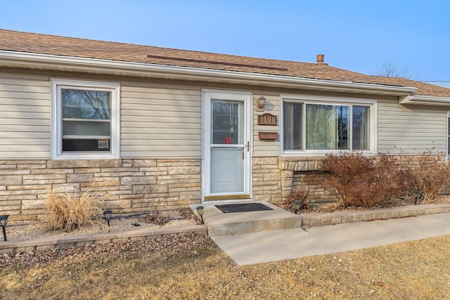 doorway to property featuring stone siding and a shingled roof