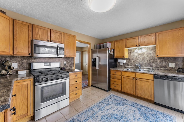 kitchen with dark countertops, backsplash, light tile patterned flooring, stainless steel appliances, and a sink