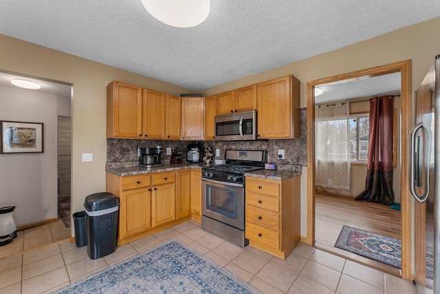 kitchen featuring light tile patterned floors, stainless steel appliances, tasteful backsplash, and a textured ceiling