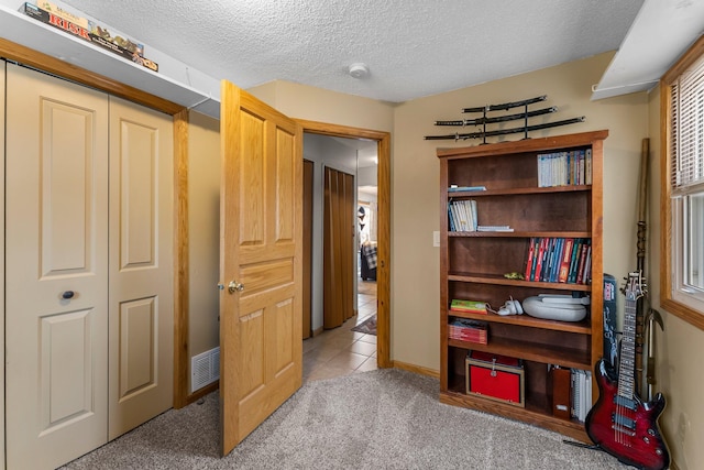 interior space featuring visible vents, light carpet, a textured ceiling, a closet, and light tile patterned floors