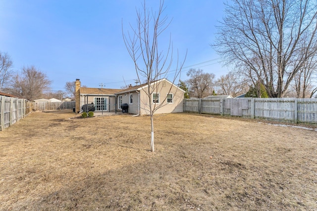 back of house featuring a yard, a fenced backyard, and a chimney