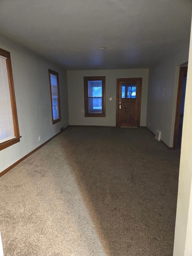 unfurnished living room featuring baseboards and dark carpet