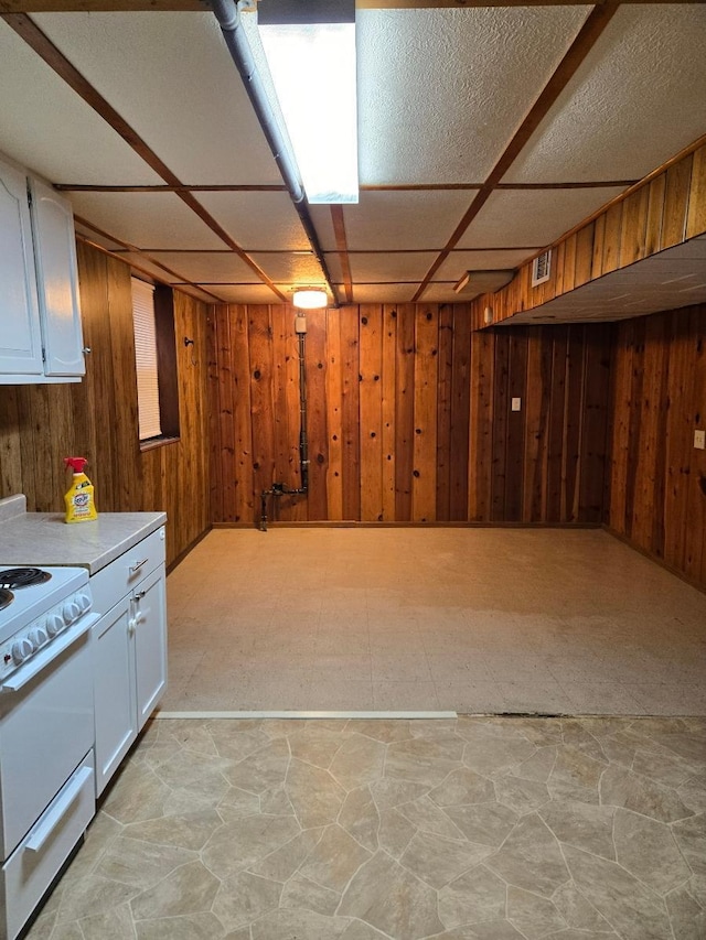 finished basement with a drop ceiling, wood walls, light floors, and visible vents