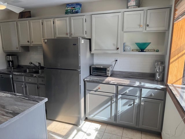 kitchen with dishwasher, gray cabinetry, a sink, and freestanding refrigerator