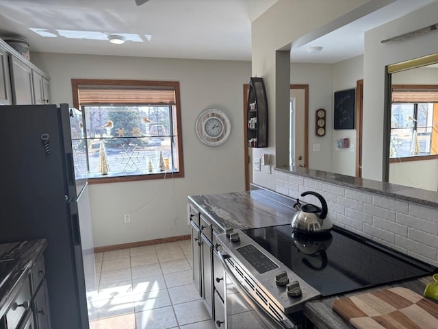 kitchen featuring tasteful backsplash, baseboards, light tile patterned floors, freestanding refrigerator, and electric range