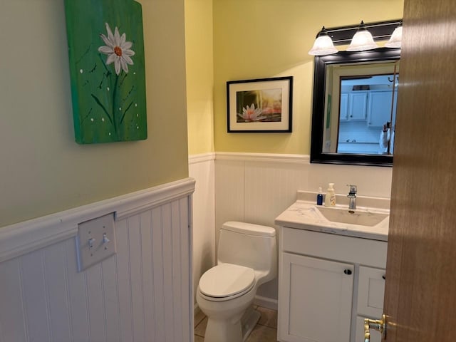 half bathroom featuring a wainscoted wall, toilet, vanity, and tile patterned flooring