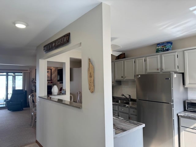 kitchen featuring decorative backsplash, carpet flooring, freestanding refrigerator, and a sink