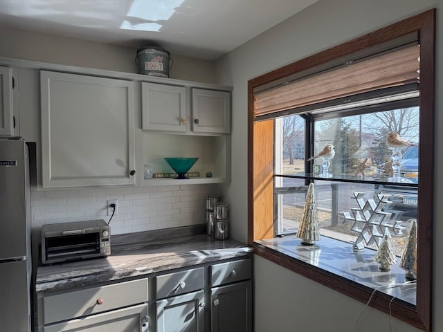 kitchen with open shelves, a toaster, freestanding refrigerator, gray cabinetry, and backsplash