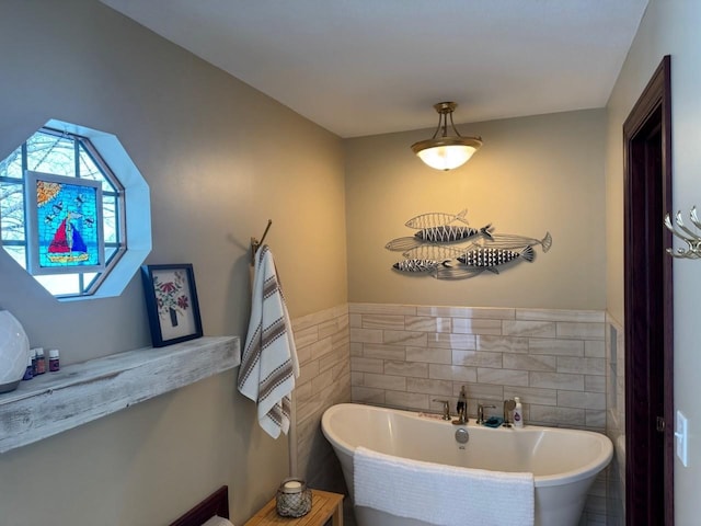 bathroom featuring a wainscoted wall, tile walls, and a freestanding tub