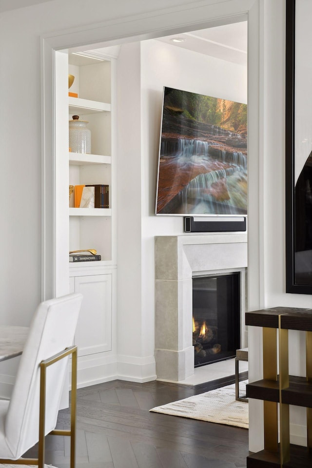 living area with a glass covered fireplace, built in shelves, baseboards, and wood finished floors