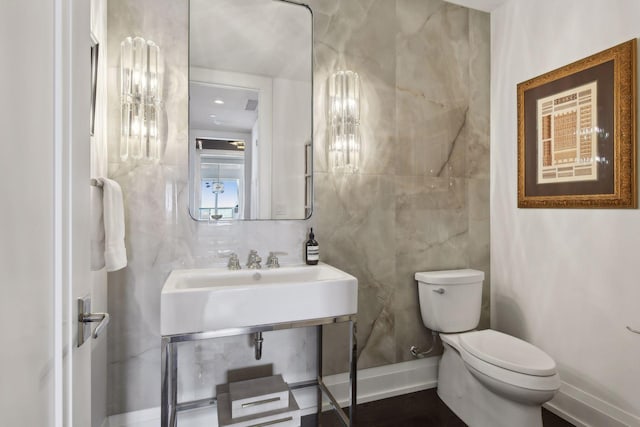 bathroom with tile walls, toilet, baseboards, and a sink