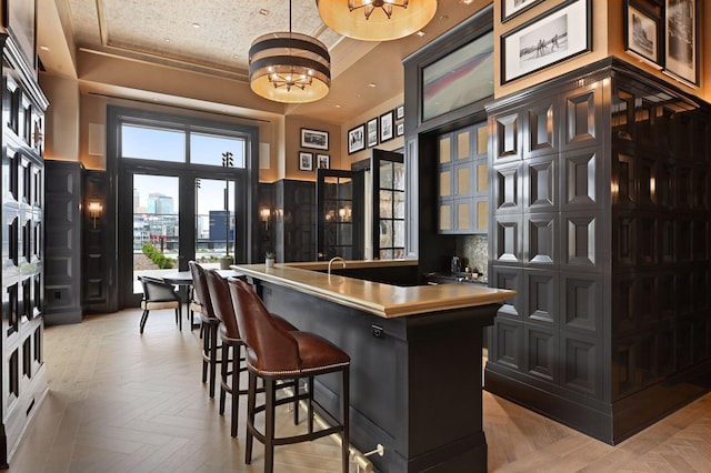 bar featuring an inviting chandelier, a tray ceiling, indoor wet bar, a city view, and a decorative wall