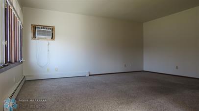 carpeted spare room with a wall mounted AC and a baseboard radiator