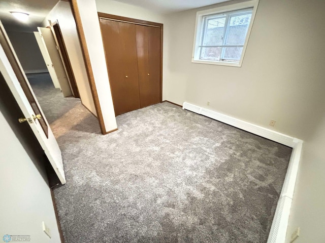 unfurnished bedroom with a closet, baseboard heating, and carpet flooring