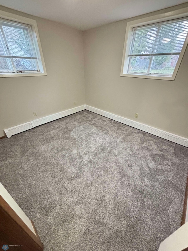 carpeted spare room featuring a baseboard heating unit, baseboards, and a wealth of natural light