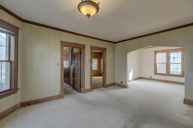 empty room with wallpapered walls, crown molding, arched walkways, and light carpet