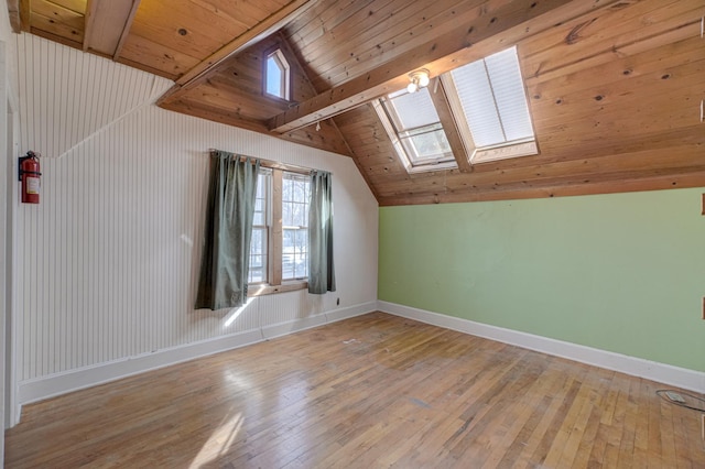 additional living space featuring vaulted ceiling with skylight, light wood-style flooring, wood ceiling, and baseboards