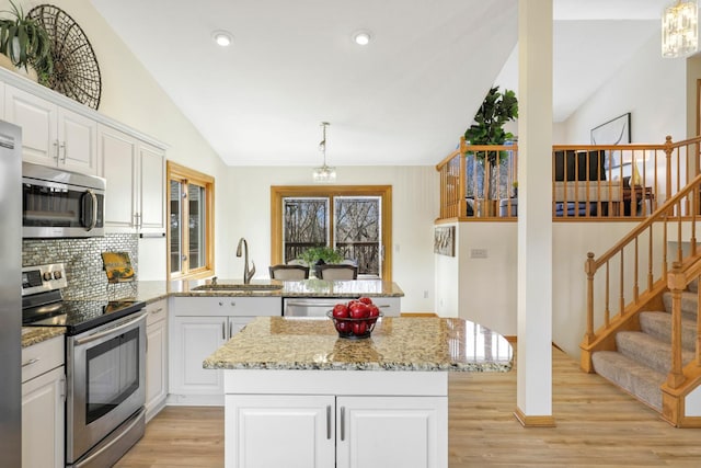 kitchen with light wood finished floors, a peninsula, stainless steel appliances, white cabinetry, and a sink