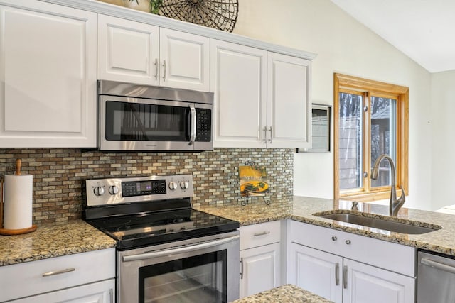 kitchen with a sink, decorative backsplash, vaulted ceiling, appliances with stainless steel finishes, and white cabinetry