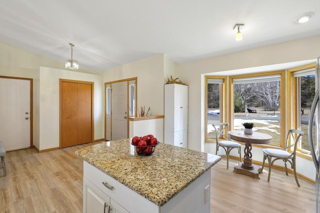 kitchen with light stone counters, light wood-style flooring, white cabinets, and a center island