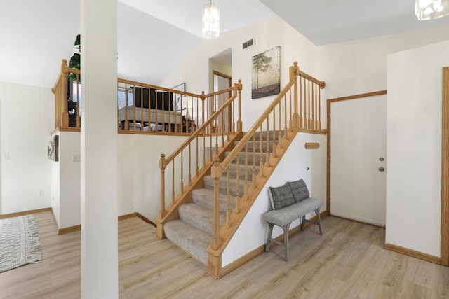 stairway with visible vents, wood finished floors, baseboards, and a towering ceiling