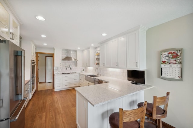 5191 Christen Ave NE, Buffalo, MN 55313 - kitchen with white cabinets, appliances with stainless steel finishes, a peninsula, and wall chimney range hood