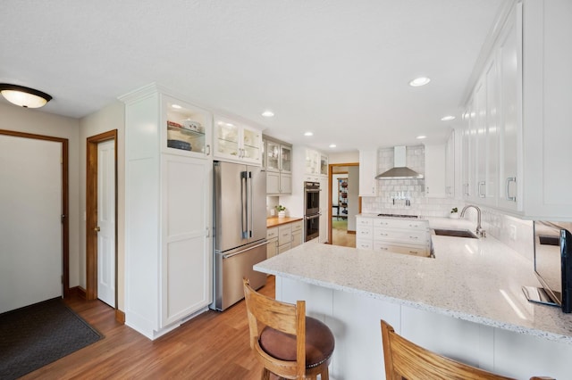 5191 Christen Ave NE, Buffalo, MN 55313 - kitchen with wall chimney range hood, appliances with stainless steel finishes, a peninsula, light wood-style floors, and a sink