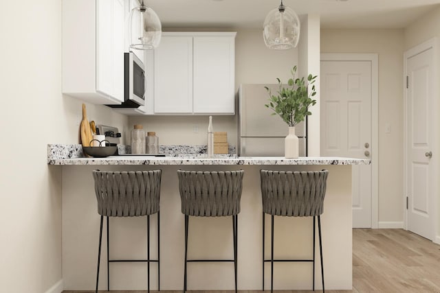 kitchen featuring light wood-type flooring, freestanding refrigerator, a breakfast bar area, white cabinets, and hanging light fixtures