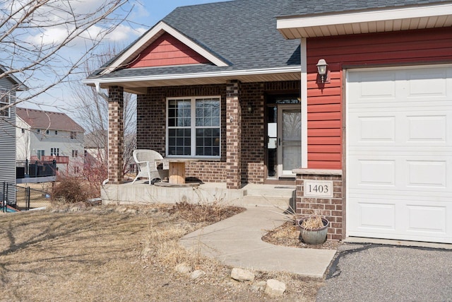 property entrance featuring brick siding, an attached garage, roof with shingles, and fence