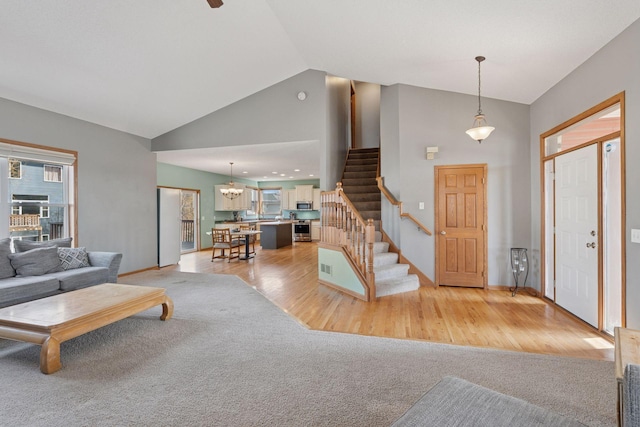 foyer with stairway, light wood finished floors, high vaulted ceiling, an inviting chandelier, and light colored carpet