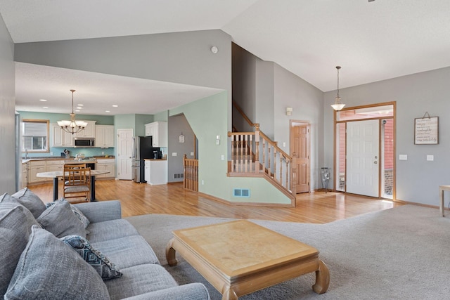 living area featuring light wood finished floors, visible vents, a chandelier, stairway, and lofted ceiling