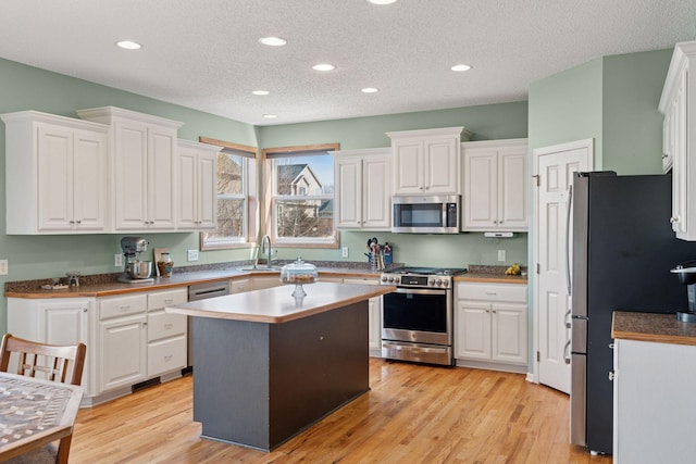 kitchen with a sink, stainless steel appliances, white cabinets, and light wood-style flooring