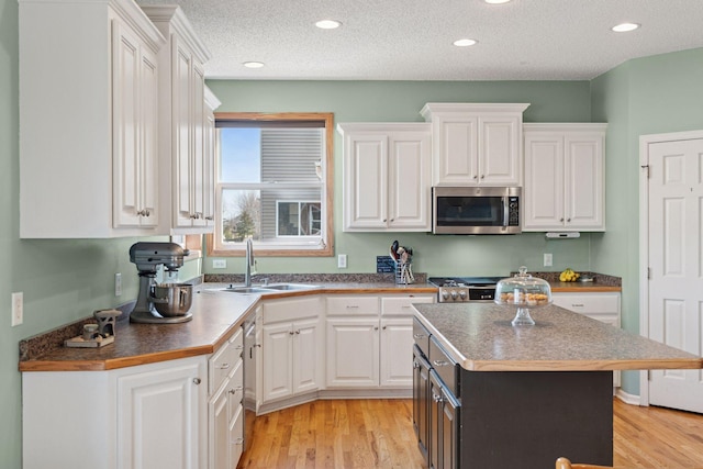 kitchen with a sink, white cabinets, light wood-type flooring, and stainless steel appliances