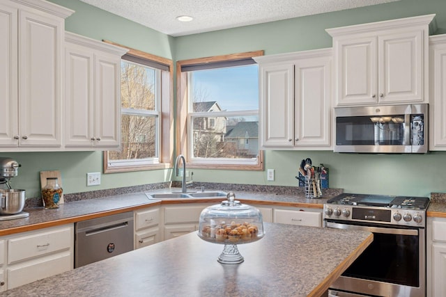 kitchen with a sink, a textured ceiling, dark countertops, stainless steel appliances, and white cabinets