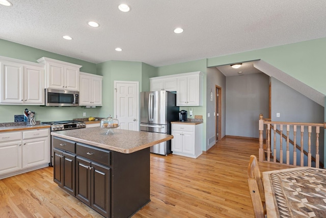 kitchen with stainless steel appliances, light wood finished floors, a center island, and white cabinetry