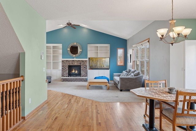 living area with built in shelves, vaulted ceiling, ceiling fan with notable chandelier, a fireplace, and wood finished floors