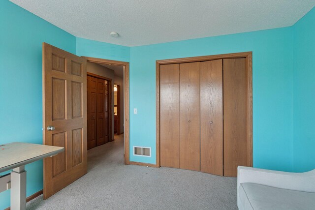 carpeted bedroom with visible vents, baseboards, a textured ceiling, and a closet