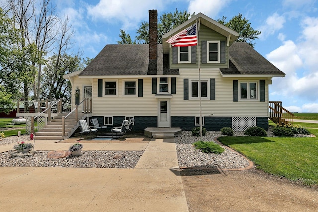 view of front of property featuring stairs, roof with shingles, a chimney, and a front lawn