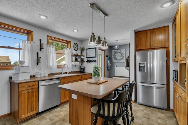 kitchen with a center island, light floors, brown cabinets, stainless steel appliances, and a sink