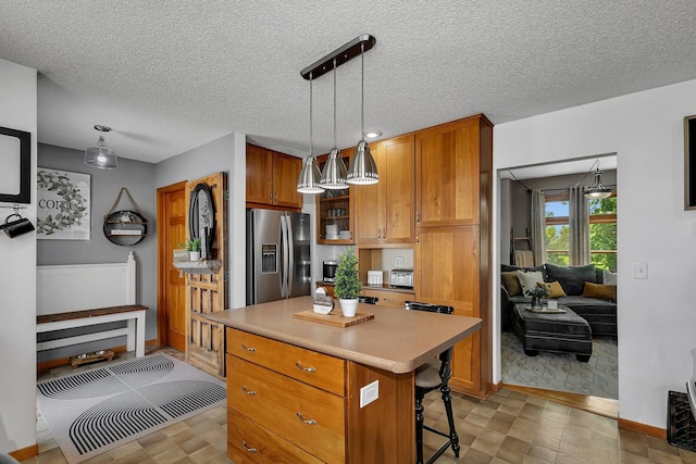 kitchen with a breakfast bar area, a kitchen island, brown cabinets, pendant lighting, and stainless steel fridge