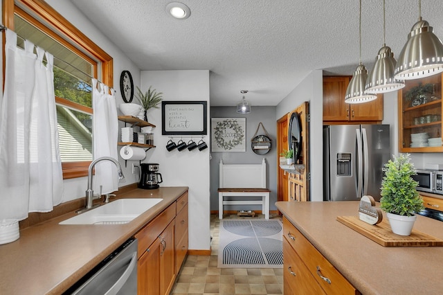 kitchen featuring a sink, decorative light fixtures, a textured ceiling, stainless steel appliances, and brown cabinetry