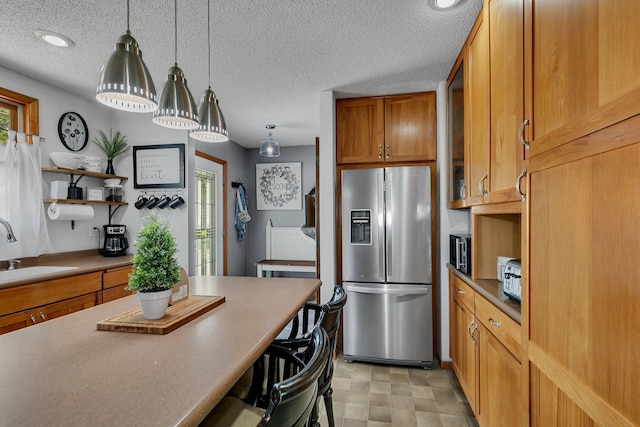 kitchen with stainless steel fridge with ice dispenser, decorative light fixtures, a breakfast bar, brown cabinetry, and a sink