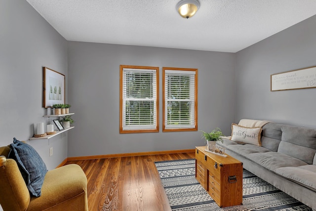 living room with a textured ceiling, baseboards, and wood finished floors