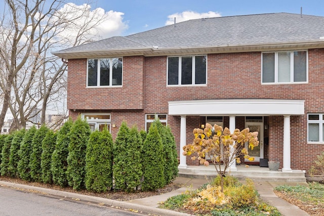 view of front of property featuring brick siding, covered porch, and a shingled roof